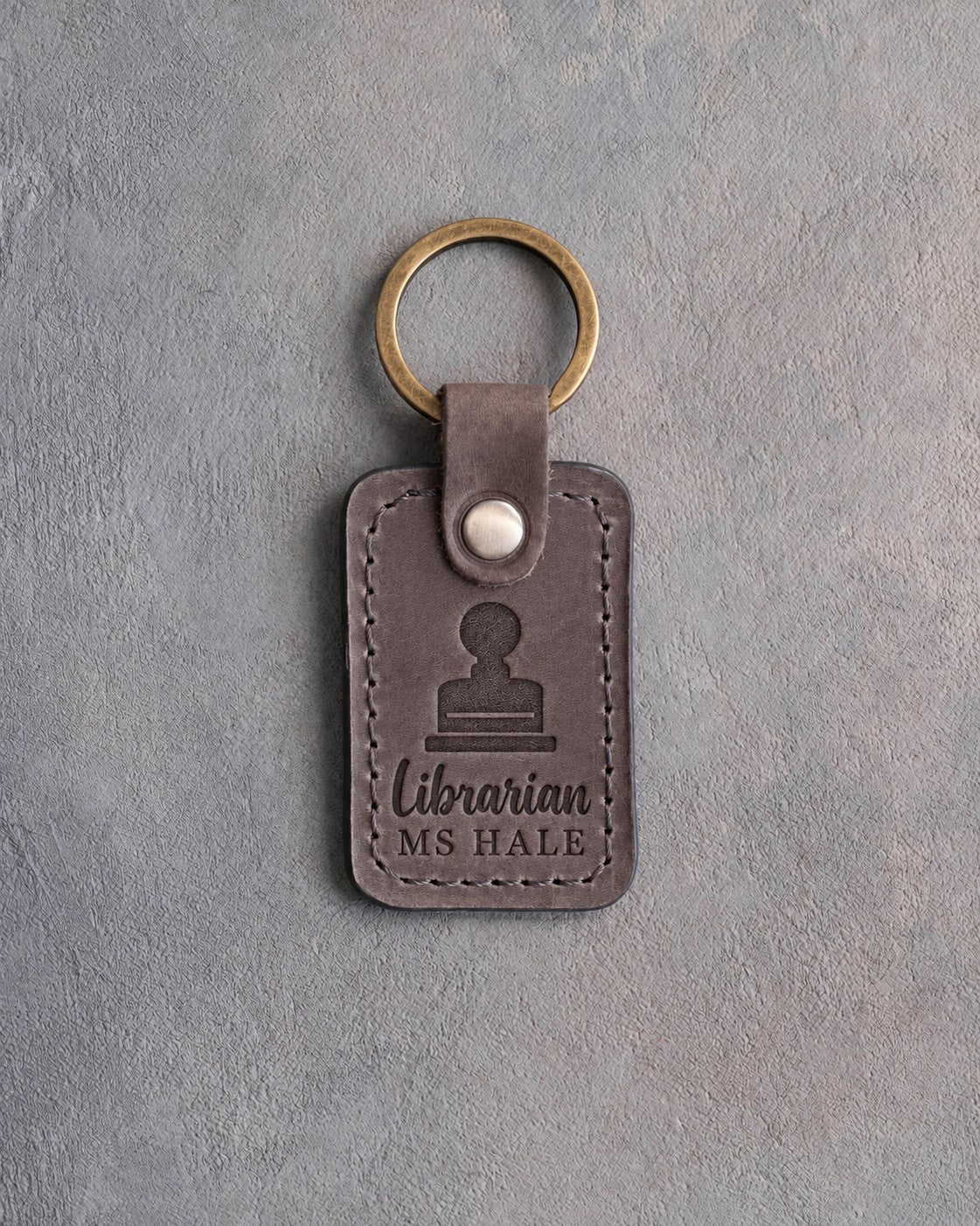Country gray leather keychain debossed with a library date stamp above Librarian and MS HALE, on gray concrete