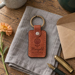 Tan Marigold October keychain beside a terracotta pot of orange marigolds on an autumn porch step