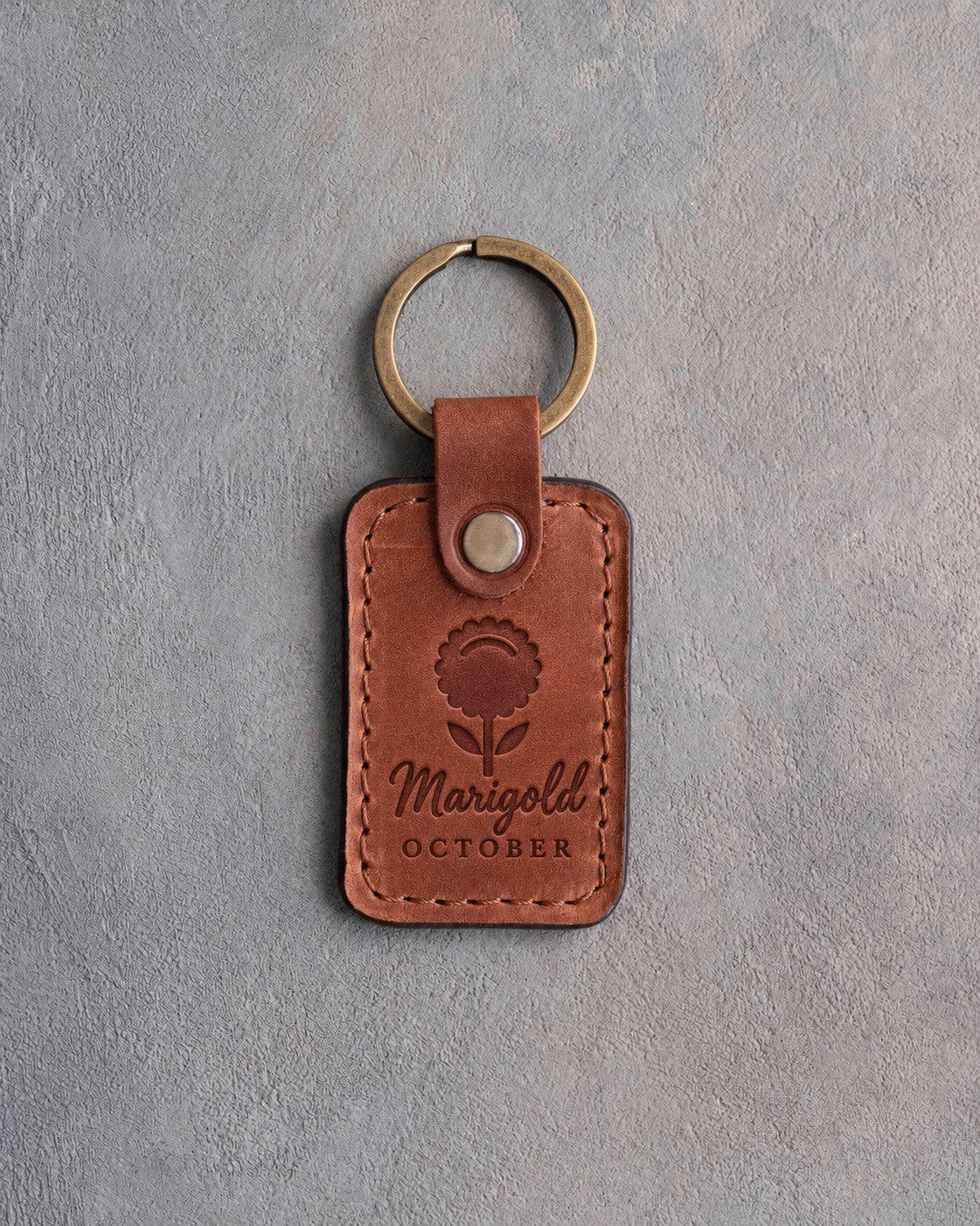Arizona tan leather keychain debossed with a marigold above Marigold and OCTOBER, on gray concrete