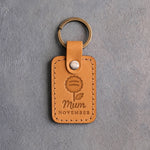 Indian Summer tan leather keychain debossed with a chrysanthemum above Mum and NOVEMBER, on gray concrete