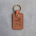Caramel leather keychain debossed with a New York State silhouette and heart above the name Olivia and NEW YORK, on gray concrete