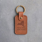 Caramel leather keychain debossed with a New York State silhouette and heart above the words Home sweet and NEW YORK, on gray concrete