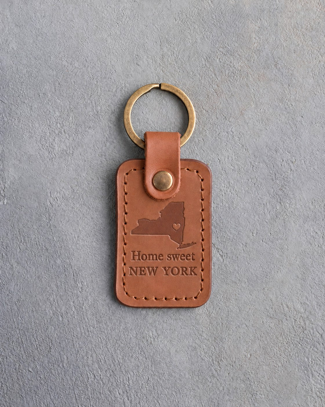Caramel leather keychain debossed with a New York State silhouette and heart above the words Home sweet and NEW YORK, on gray concrete