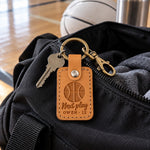 Next Play keychain in golden brown leather clipped to a player's gym bag on a hardwood court
