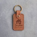 Caramel leather keychain debossed with a gable-front house above Our place and SINCE 2023, on gray concrete
