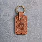 Caramel leather keychain debossed with a gable-front house above the words Our place and HOME SWEET HOME, on gray concrete