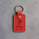 Poppy red leather keychain debossed with a poppy above Poppy and AUGUST, on gray concrete