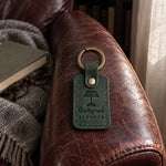 Green Reading nook ELEANOR keychain on the arm of a worn leather armchair with a wool throw behind