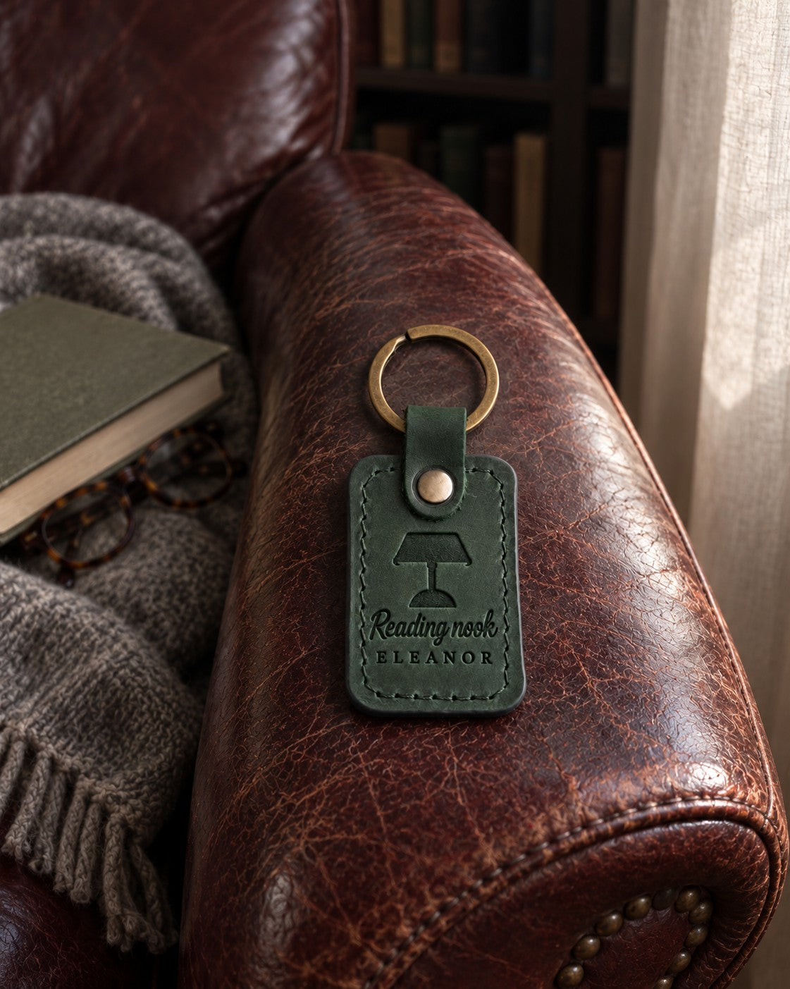 Green Reading nook ELEANOR keychain on the arm of a worn leather armchair with a wool throw behind