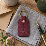 Wine red Rose June keychain on a ring of keys beside a single red rose on a white linen tablecloth