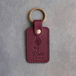 Sangria red leather keychain debossed with a rosebud above Rose and JUNE, on gray concrete