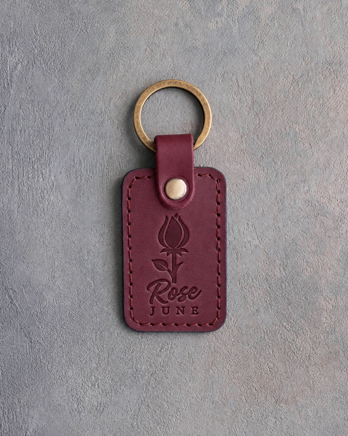 Sangria red leather keychain debossed with a rosebud above Rose and JUNE, on gray concrete