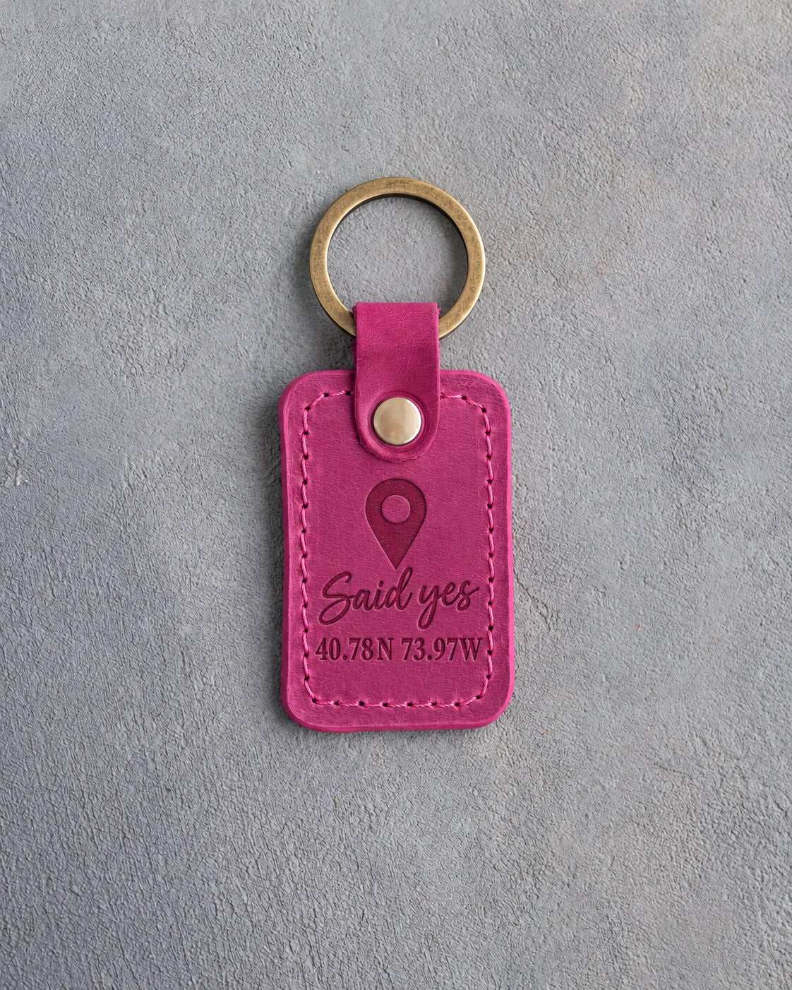 Fuchsia pink leather keychain debossed with a map pin above Said yes and 40.78N 73.97W, on gray concrete