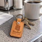 Golden tan Snowbird keychain on condo keys resting on a patio table beside a potted cactus in winter sun