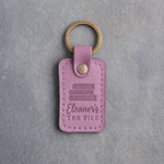 Lilac leather keychain debossed with a pile of three books above Eleanor's and TBR PILE, on gray concrete