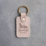 Gray sand leather keychain debossed with a sitting cat beside a loafing cat above the names Luna & Leo and STAFF
