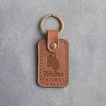 Caramel leather keychain debossed with a pair of dog tags above the name Walter and VETERAN, on gray concrete