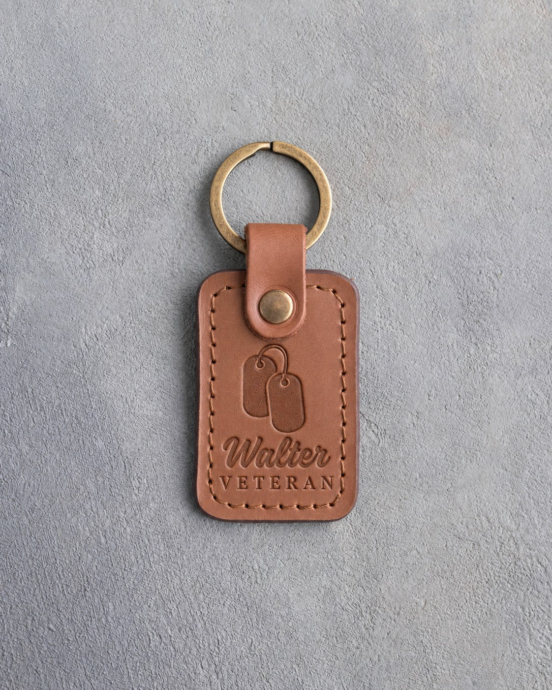 Caramel leather keychain debossed with a pair of dog tags above the name Walter and VETERAN, on gray concrete
