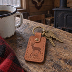 Cole WHITETAIL keychain in caramel leather on a key ring resting on a camouflage jacket sleeve in morning light