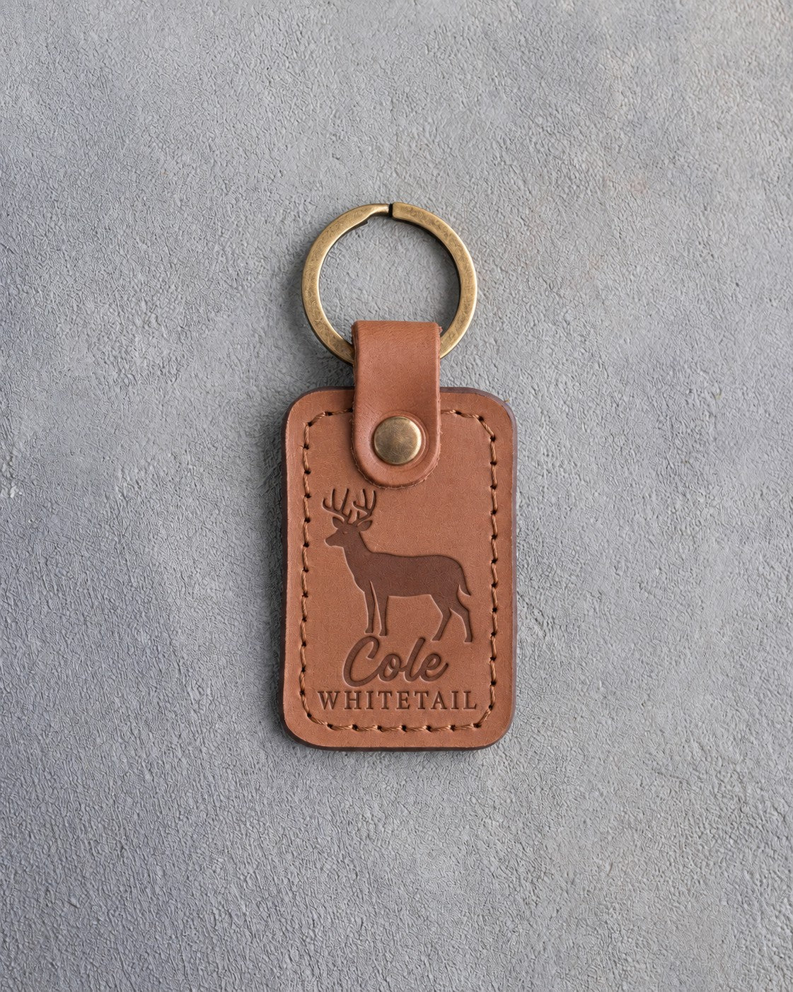Caramel leather keychain debossed with a whitetail buck above the name Cole and WHITETAIL, on gray plaster