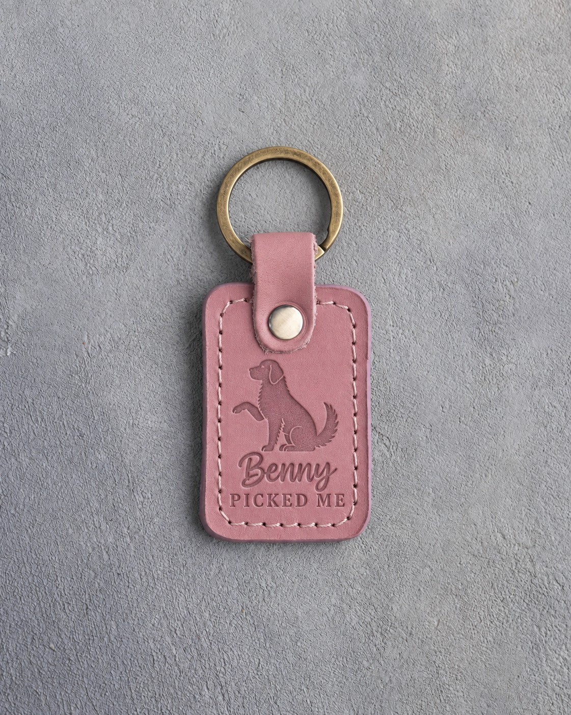 Parisian Blossom pink leather keychain debossed with a dog raising one paw above Benny and PICKED ME, on gray concrete