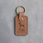 Caramel leather keychain debossed with a chihuahua silhouette and the words Picks ONE PERSON, on gray concrete