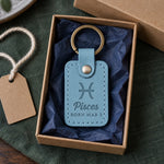 Turquoise Pisces keychain on a key ring resting on a beach bag beside a pair of sunglasses