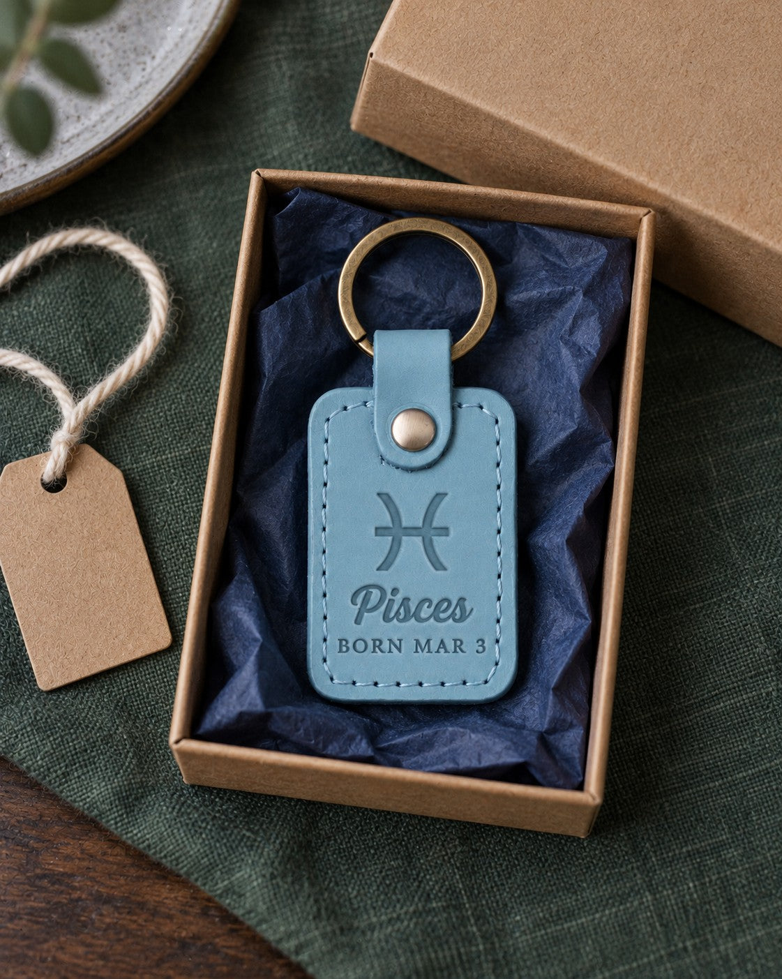 Turquoise Pisces keychain on a key ring resting on a beach bag beside a pair of sunglasses