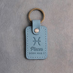 Turquoise leather keychain debossed with the Pisces zodiac glyph above Pisces and BORN MAR 3, on gray concrete