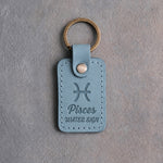 Turquoise leather keychain debossed with the Pisces zodiac glyph above Pisces and WATER SIGN, on gray concrete