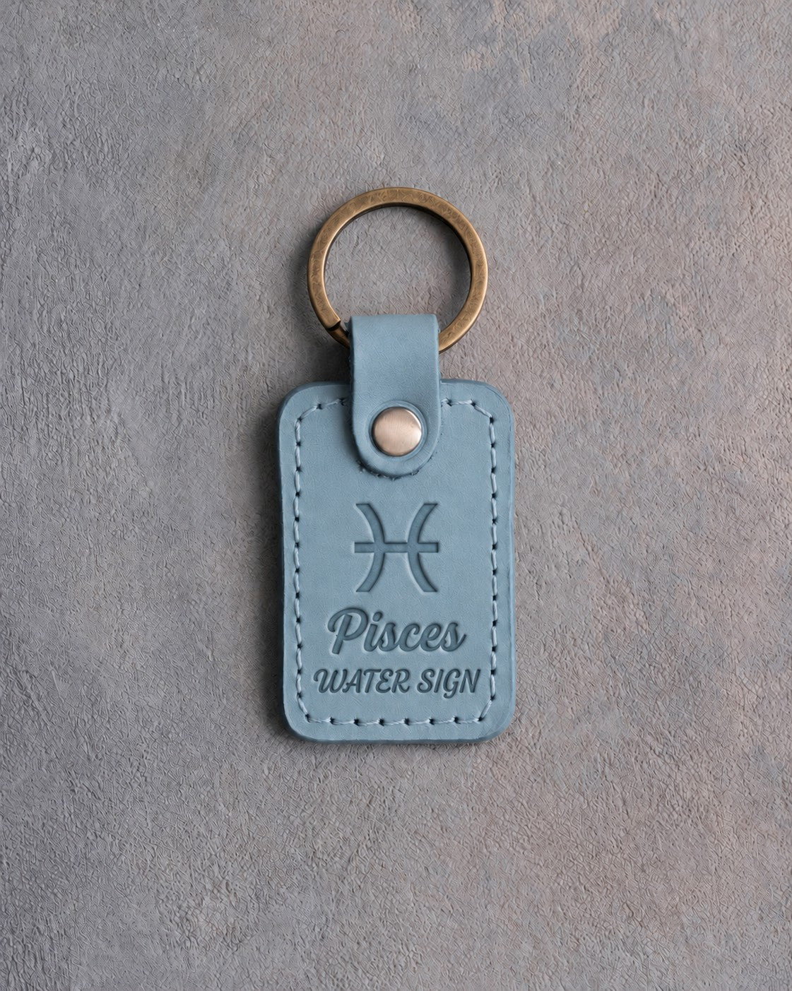 Turquoise leather keychain debossed with the Pisces zodiac glyph above Pisces and WATER SIGN, on gray concrete