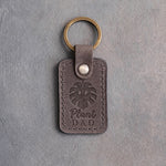 Country gray leather keychain debossed with a monstera leaf above the words Plant DAD, on gray concrete