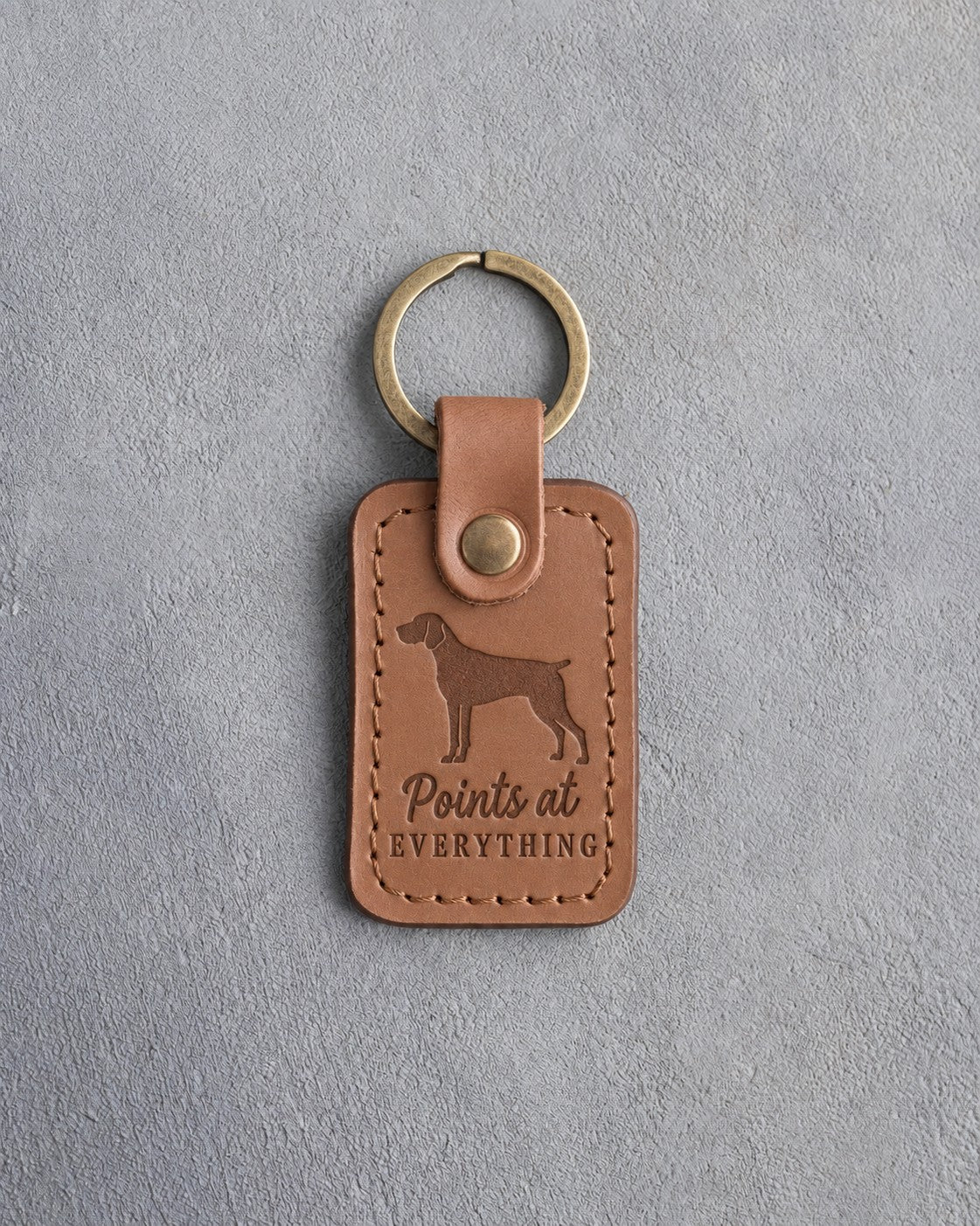 Caramel leather keychain debossed with a German Shorthaired Pointer silhouette and the words Points at EVERYTHING, on gray concrete