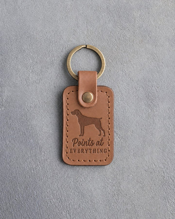 Caramel leather keychain debossed with a German Shorthaired Pointer silhouette and the words Points at EVERYTHING, on gray concrete