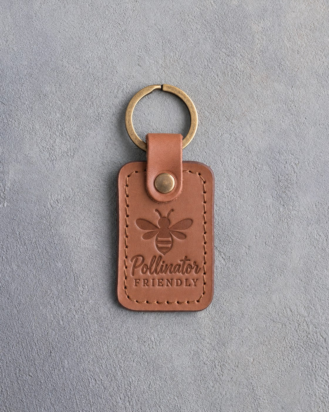 Caramel leather keychain debossed with a honeybee above Pollinator FRIENDLY, on gray concrete