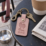 Blush pink Pom Mom leather keychain placed in a warm everyday setting