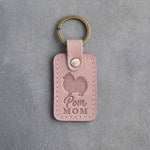 Blush pink leather keychain debossed with a Pomeranian silhouette and the words Pom MOM, on gray concrete