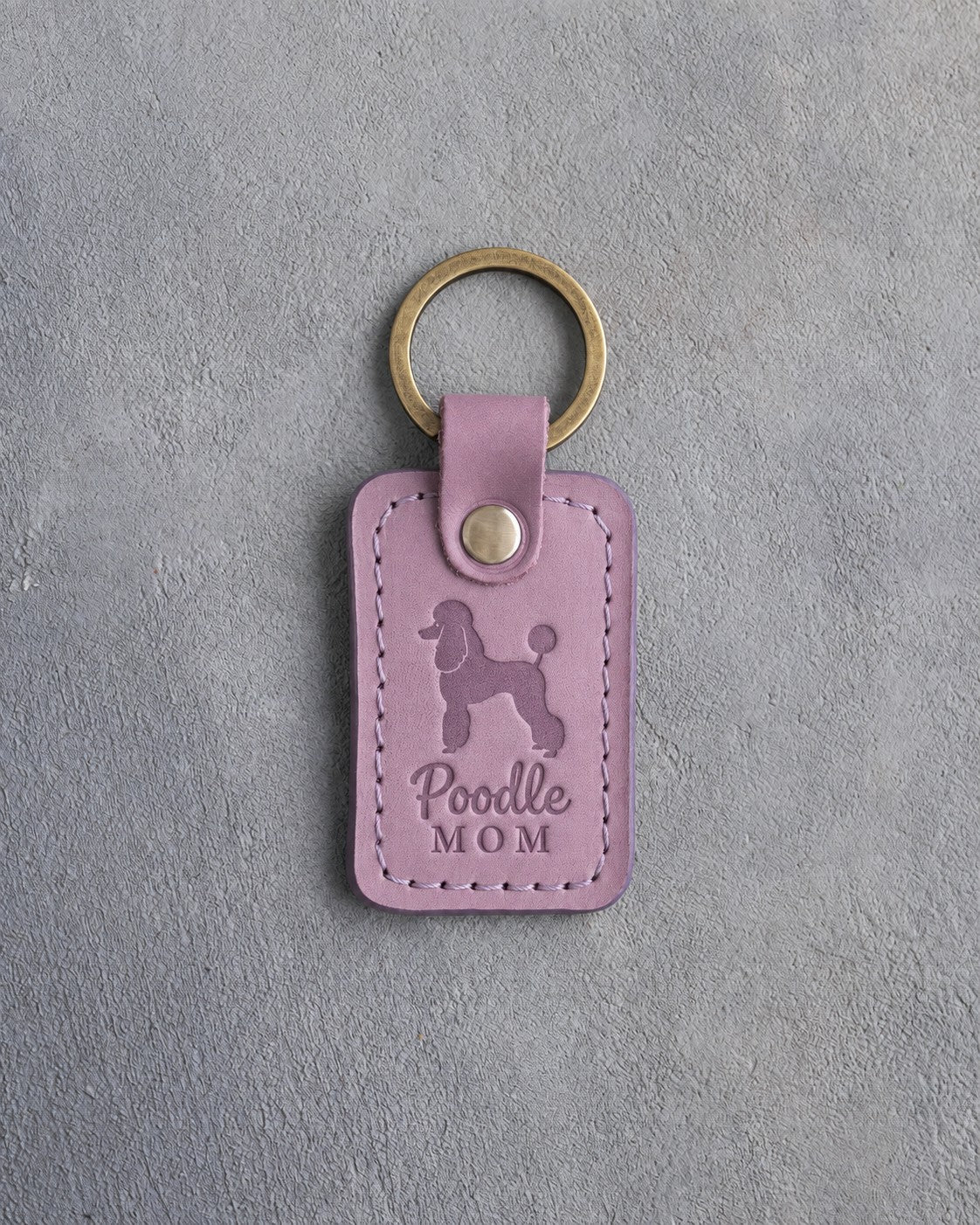 Lilac leather keychain debossed with a Poodle silhouette and the words Poodle MOM, on gray concrete