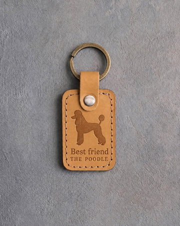 Indian Summer tan leather keychain debossed with a Poodle silhouette above Best friend and THE POODLE, on gray concrete