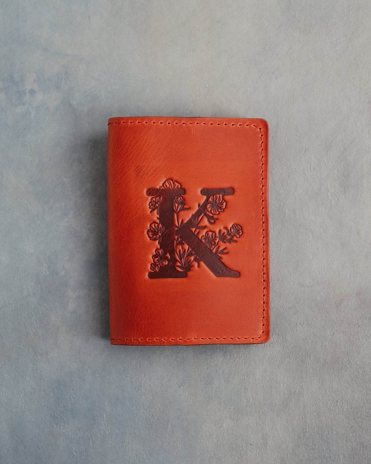 Poppy Red leather passport cover with a large floral initial K pressed into the front