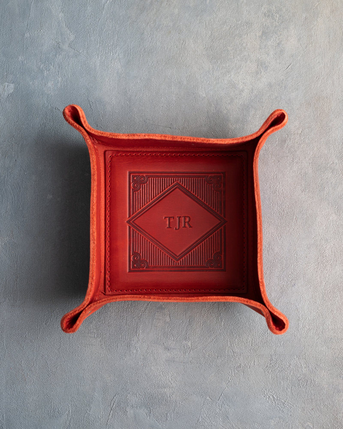 Poppy Red leather valet tray with snapped corners and the initials TJR pressed into the diamond frame, seen from above