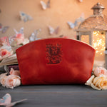 Poppy red initial makeup pouch with a floral monogram, staged among pale roses on a slate table