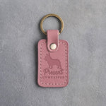 Parisian Blossom pink leather keychain debossed with a French bulldog and the words Present UNWRAPPER, on gray concrete
