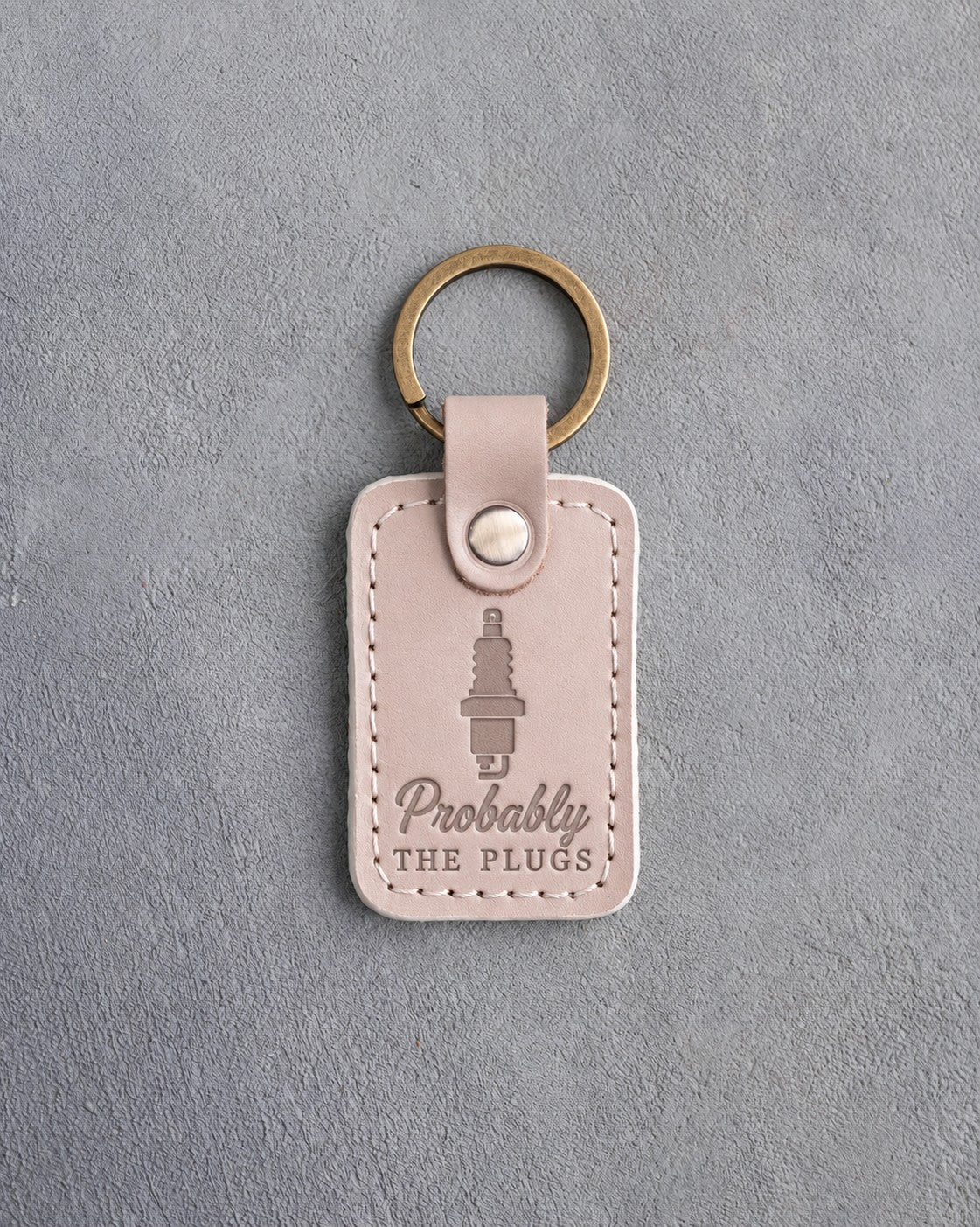 Gray sand leather keychain debossed with a spark plug above Probably and THE PLUGS