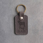 Country gray leather keychain with a debossed pug silhouette and Pug DAD lettering, on gray concrete