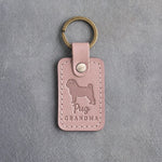 Blush pink leather keychain debossed with a pug silhouette and the words Pug GRANDMA, on gray concrete