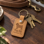 Tan Pug Life Chose Me keychain lying with brass keys on a walnut table in warm afternoon light