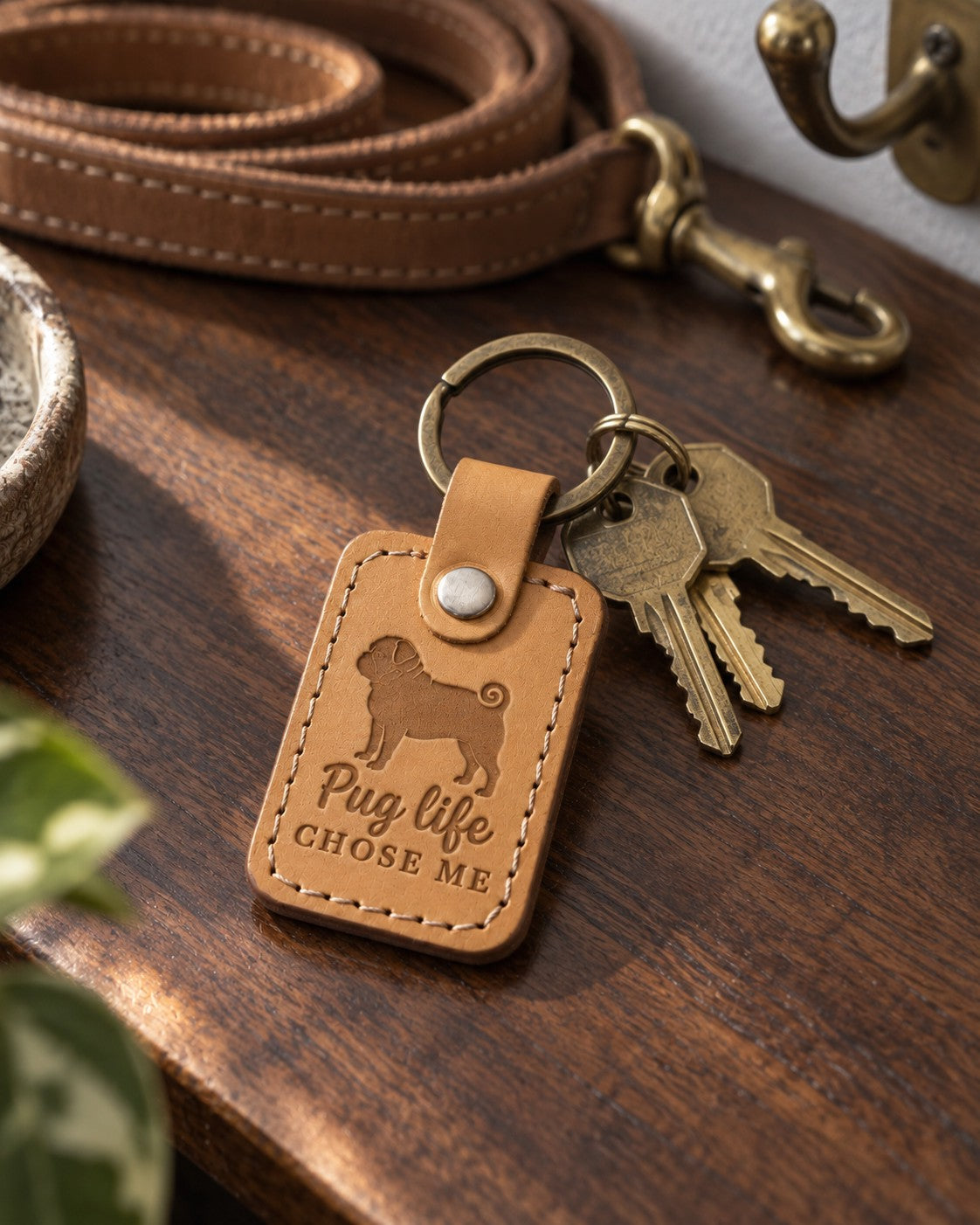 Tan Pug Life Chose Me keychain lying with brass keys on a walnut table in warm afternoon light