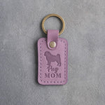 Lilac leather keychain debossed with a pug silhouette and the words Pug MOM, lying on gray concrete