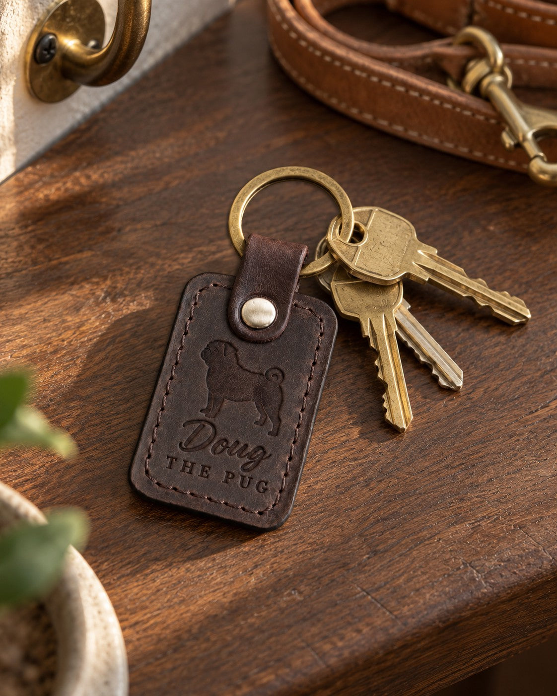Doug the Pug keychain in dark brown leather with brass house keys on a walnut entry table